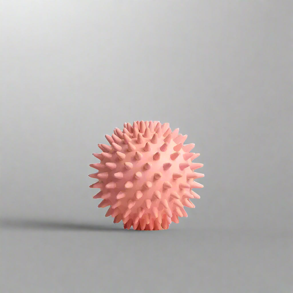 Pink spiky massage ball by FitSupplyZone on white pedestal with curved pink background
