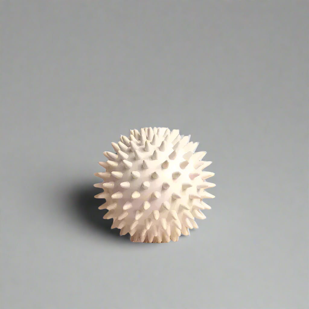 White spiky massage ball from FitSupplyZone on a white pedestal with beige geometric background
